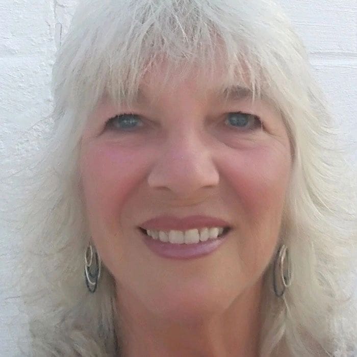 A close-up portrait of a smiling woman with shoulder-length blond hair, against a white background.